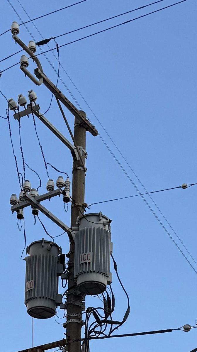 1本の電柱に柱上変圧器が2台ならんで取り付けられている写真。どちらも縦にひだの入った灰色の円筒形で、側面に赤い数字が書かれている。上の腕金にはがいしが並び、引き下げ線が変圧器へつながっている