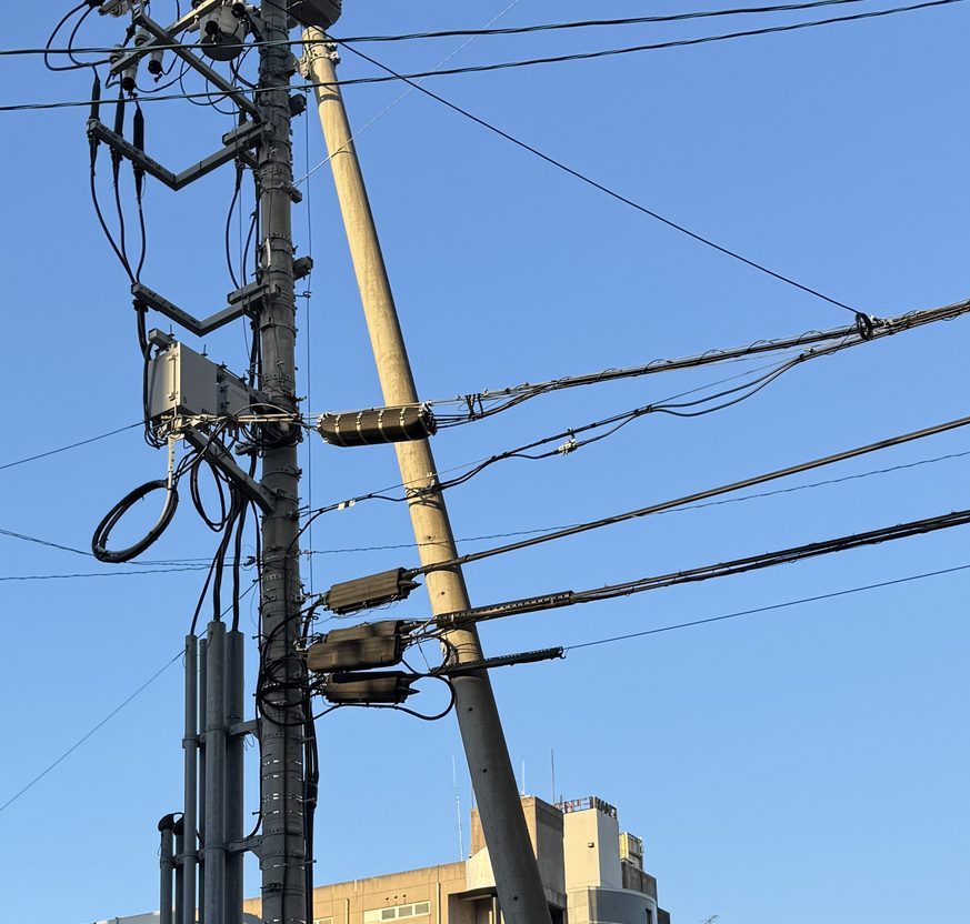 電柱にもう1本の柱が斜めに寄りかかっている支柱の写真。手前の柱には腕金や機器が付き、柱に沿って太い管が何本も立ち上がっている。斜めの柱は上のほうで電柱に固定されている